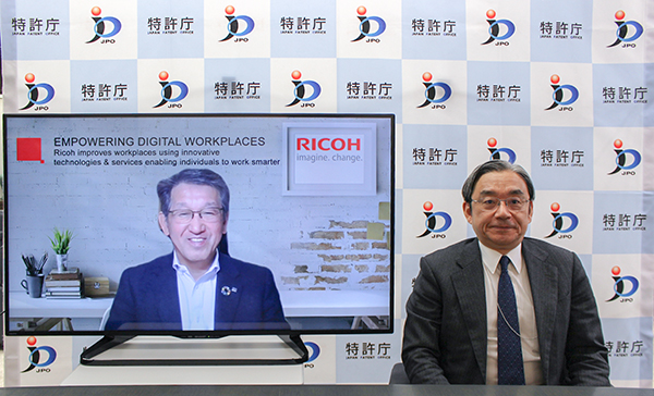 （写真）糟谷長官と、モニタに映る山下社長