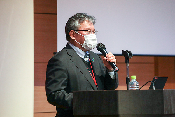 （写真）マイクを手に話す三重大学大学院　地域イノベーション学研究科長　小林氏
