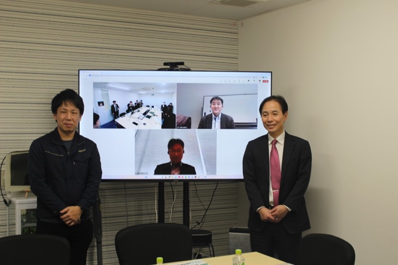 (写真1)株式会社エネコートテクノロジーズとの意見交換 - 加藤代表取締役社長執行役員CEO(モニター内右上)、堀内取締役執行役員CTO(モニター内下)、小田執行役員管理本部長(左)、安田技監(右)